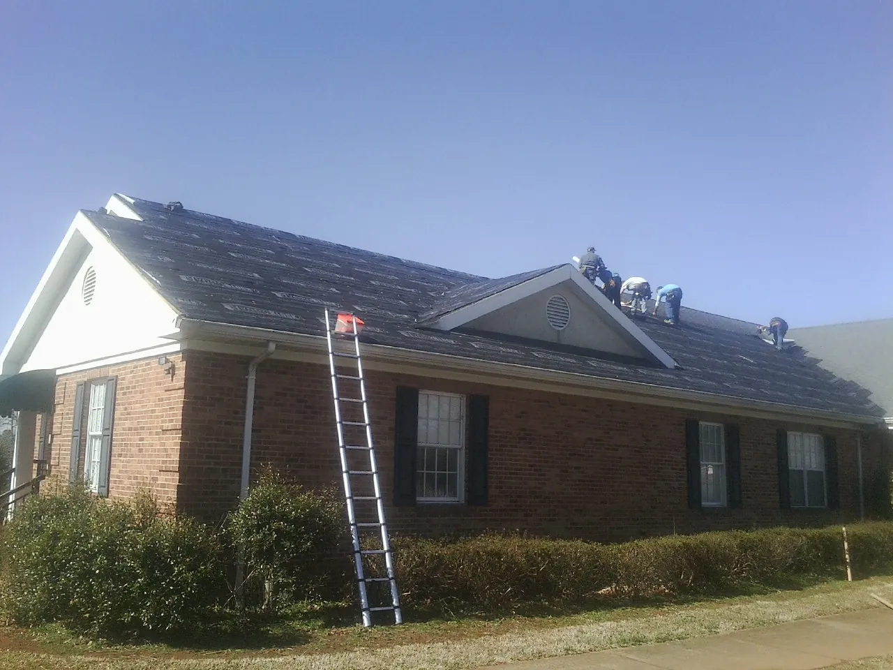 Crew tearing shingles off a brick ranch roof with a ladder set — Emergency Roof Repair work by our crew in Reardan