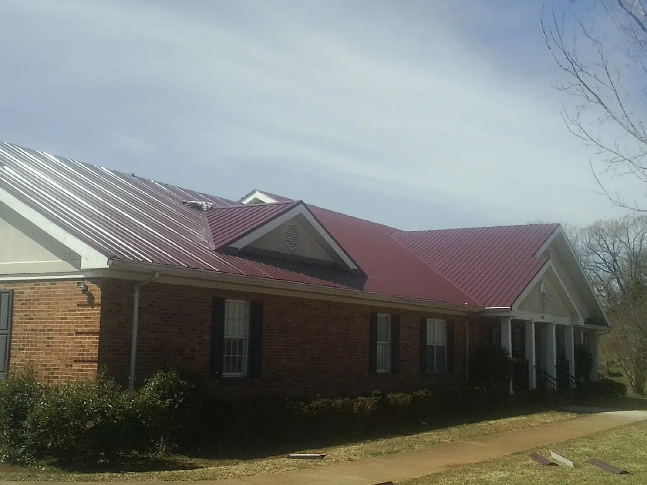 Red metal roof with gabled entries on a long brick building, from a Hail Damage Roof Repair job in Reardan