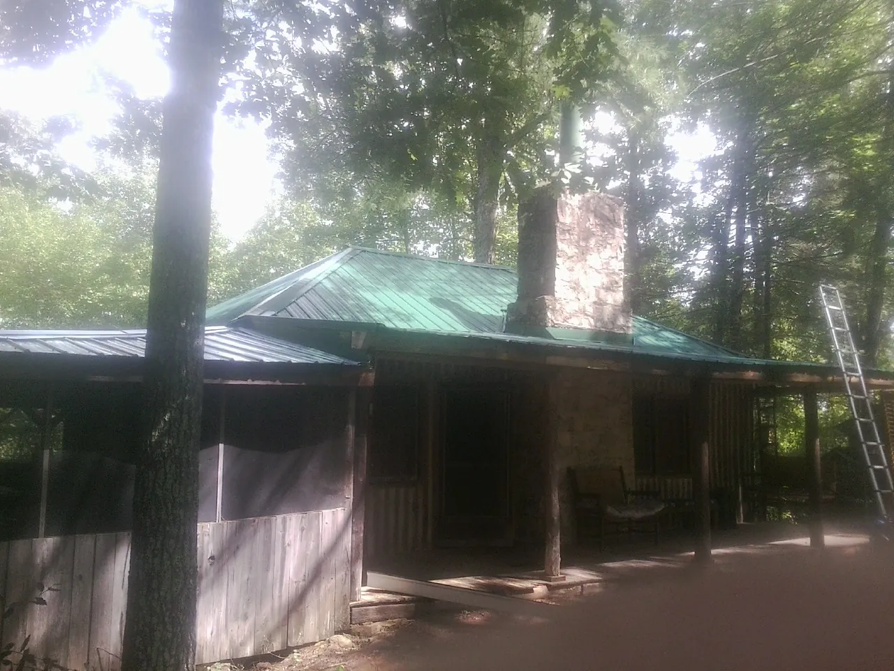 Green metal roof and stone chimney above a log cabin porch in Reardan