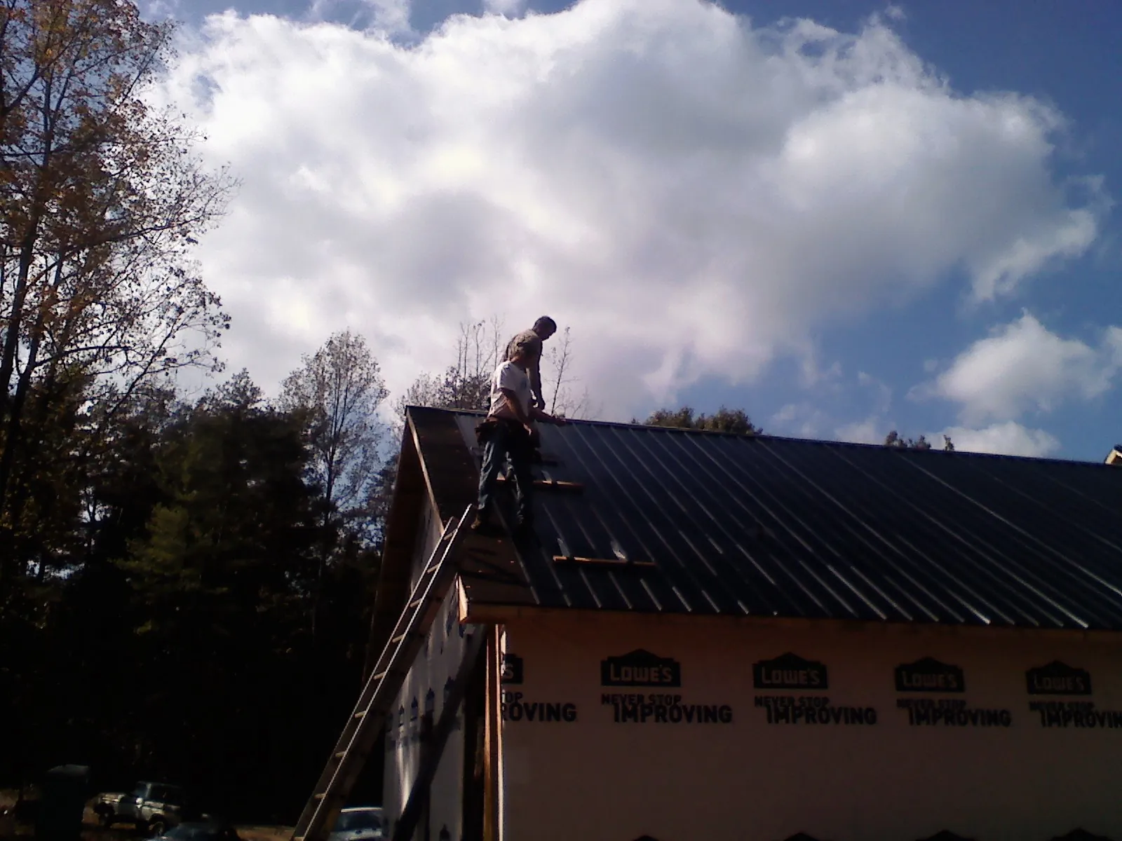 Roofer fastening dark metal panels high against a cloudy sky, from a Roof Inspection job in Reardan