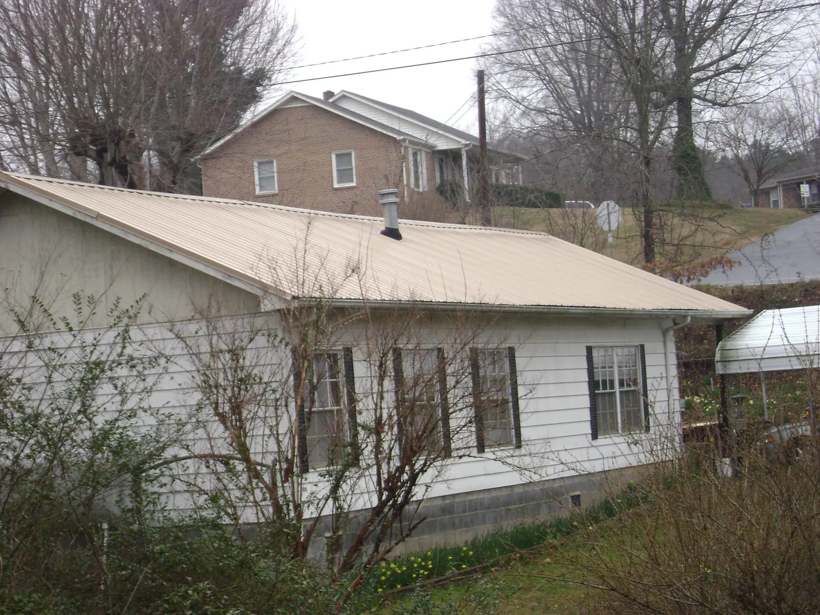 Tan metal roof on a white sided house set into a hillside — Commercial Roofing by Roofing Brothers in Reardan